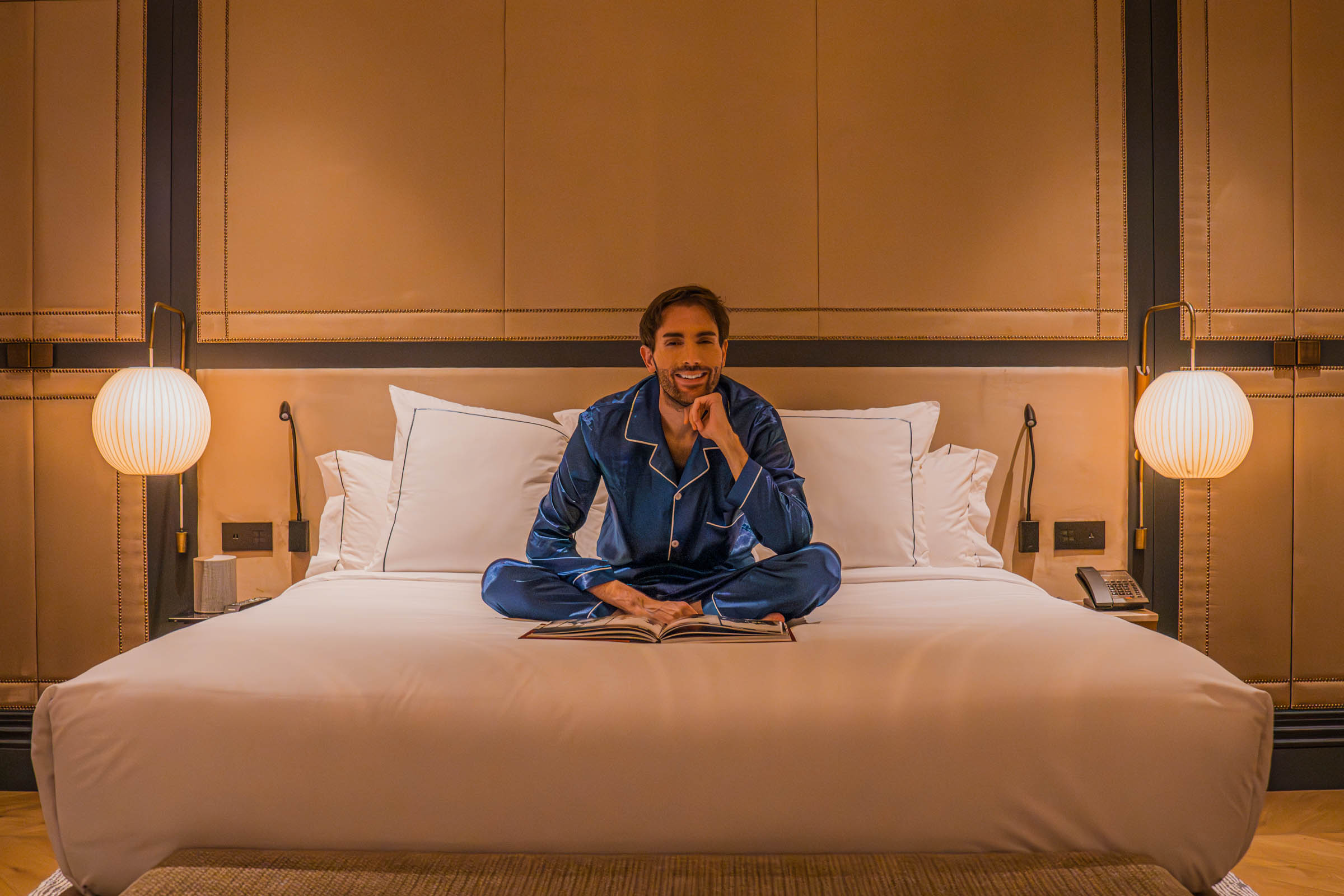 Marko Tadic (Mr.M) sits on the bed in the luxurious Master Suite bedroom at the CoolRooms Palacio de Atocha Hotel with a king-size bed