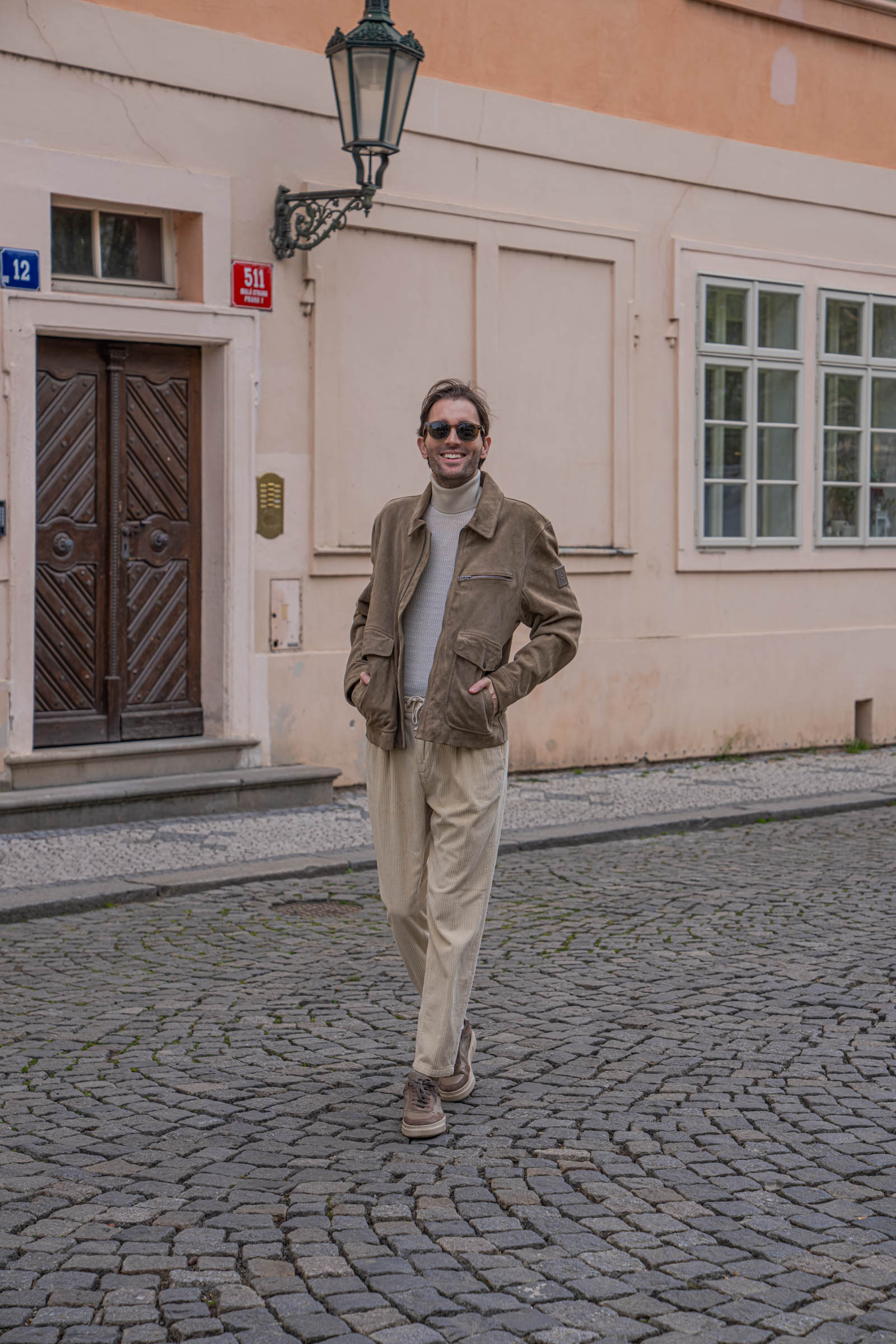Marko Tadić, founder of Mr.M by Marko Tadić blog, in a Belstaff suede jacket and Loro Piana cream corduroy trousers on a cobblestone street of Prague's Malá Strana.