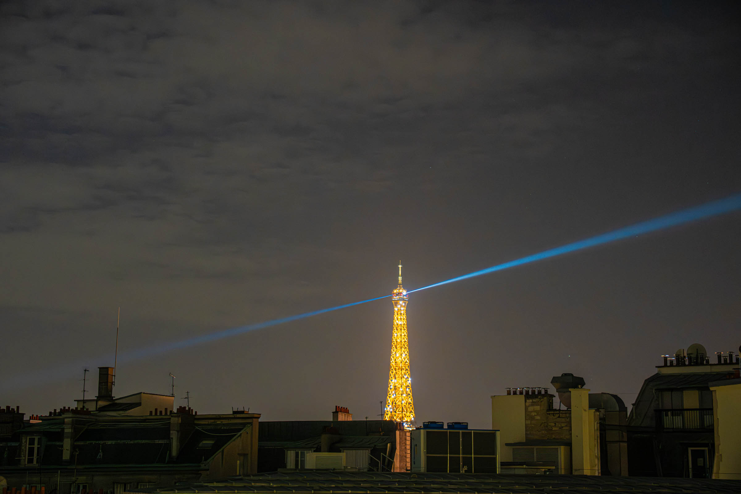 Illuminated Eiffel Tower with its sweeping searchlight beam over Paris rooftops at night, seen from Hôtel Napoléon Paris, photo by Marko Tadić, founder of Mr.M by Marko Tadić blog