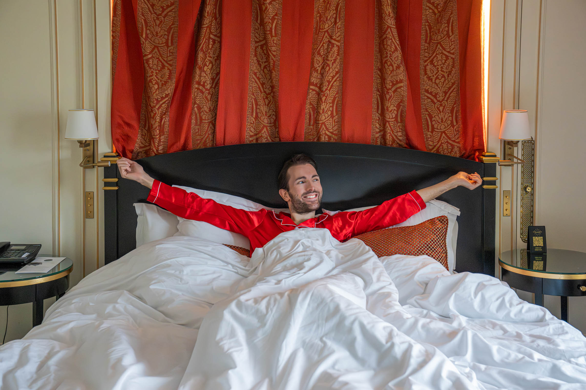 Marko Tadic relaxing in red silk pyjamas in the Suite Avenue bed beneath the red and gold canopy at Hôtel Napoléon Paris, photo by Marko Tadić, founder of Mr.M by Marko Tadić blog