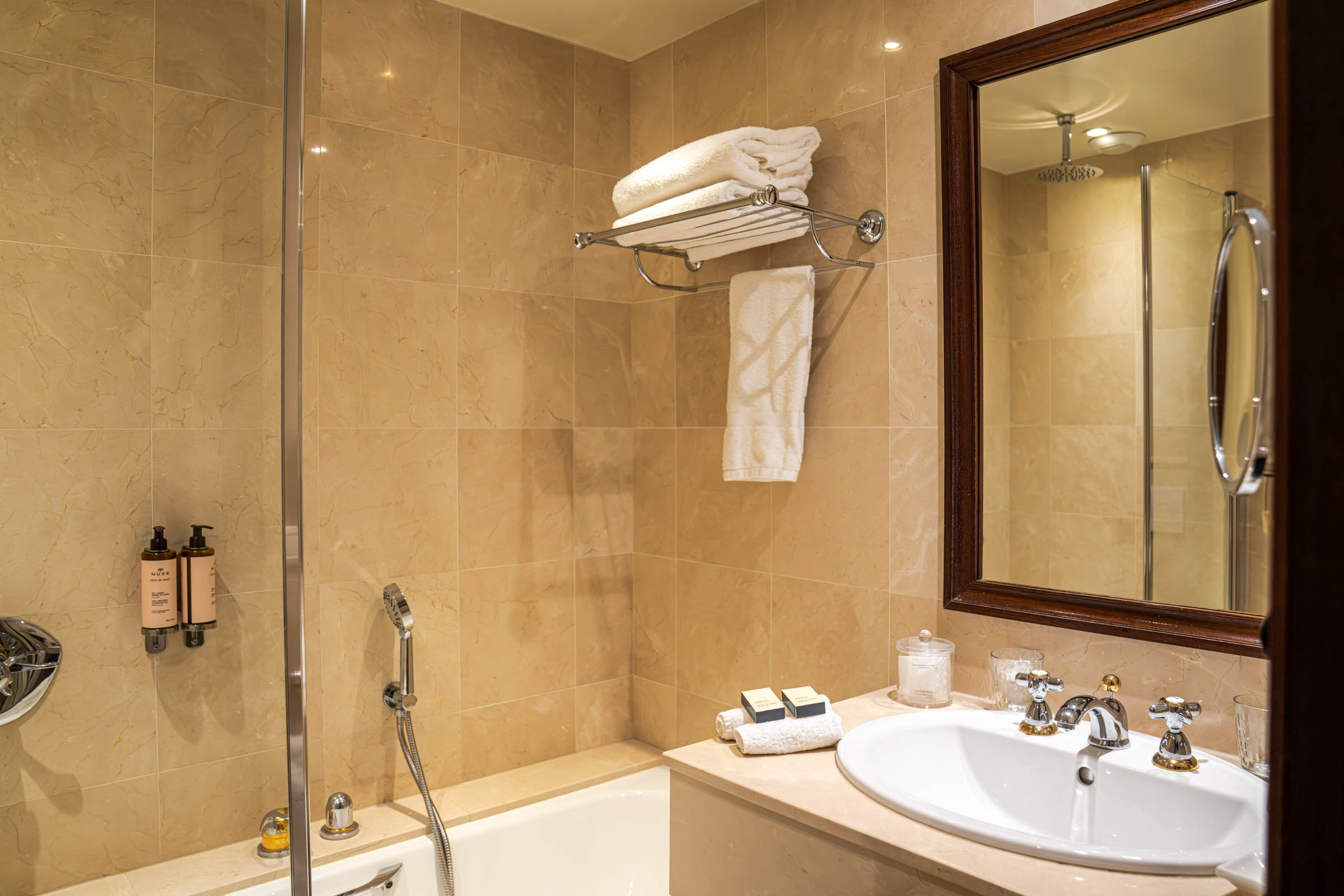 Beige marble bathroom at Hôtel Napoléon Paris with a glass shower screen, plush white towels and a wood-framed mirror, photo by Marko Tadić, founder of Mr.M by Marko Tadić blog