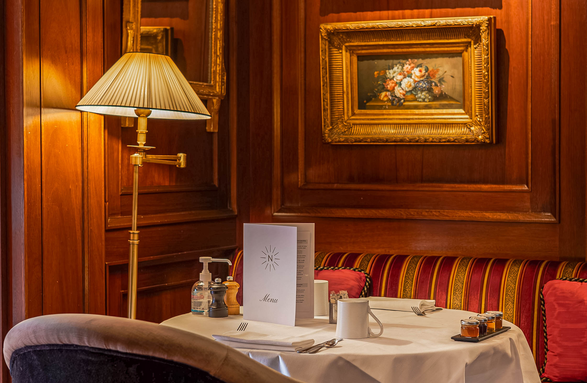 Wood-paneled dining corner at Hôtel Napoléon Paris with a gilt-framed floral painting, brass lamp and a set breakfast table, photo by Marko Tadić, founder of Mr.M by Marko Tadić blog