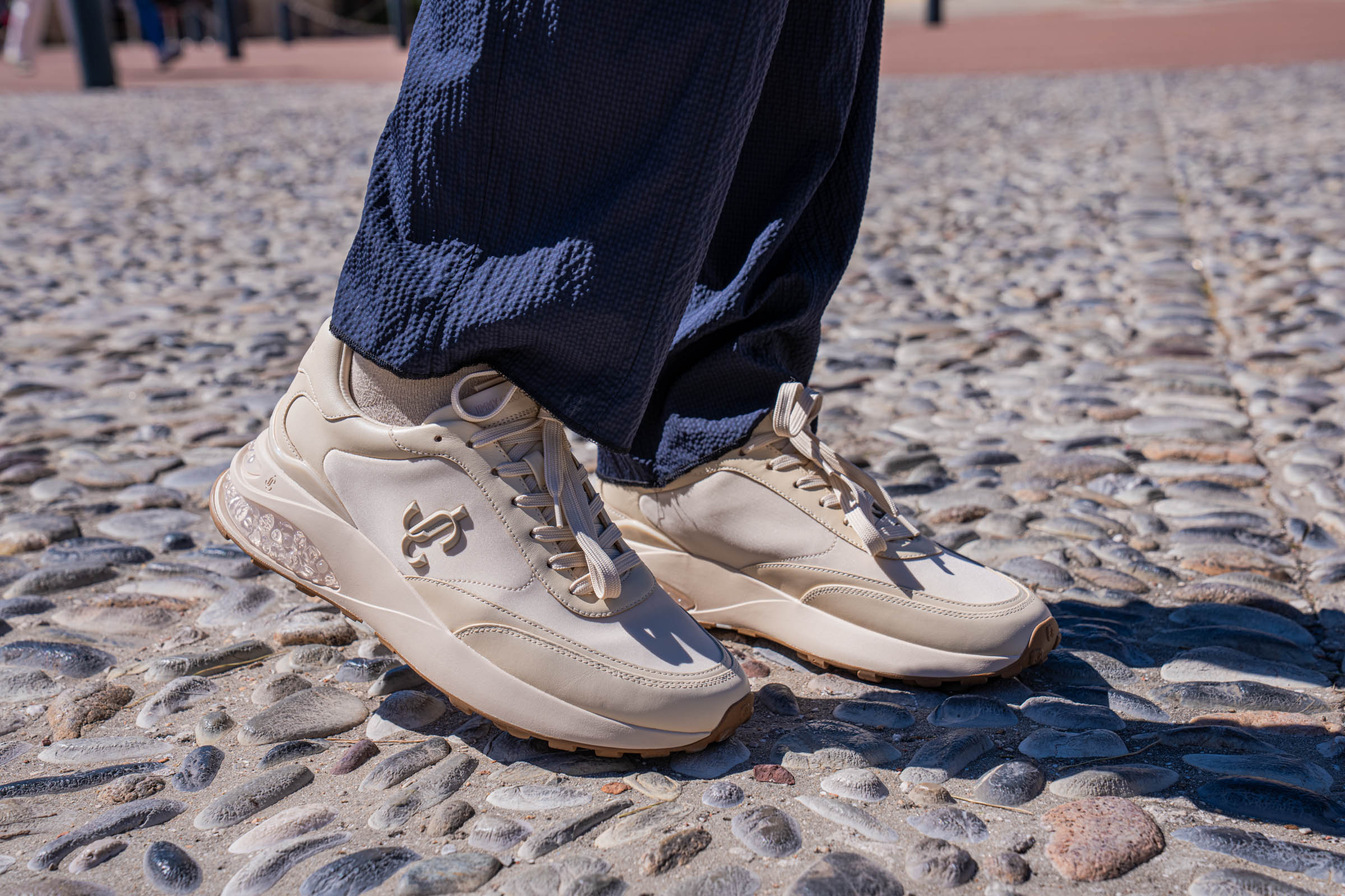 Close up of the Jimmy Choo Memphis lace up sneakers in natural beige leather with JC emblem and gum sole worn by Marko Tadić, founder of the Mr.M blog, on Monaco's pebble mosaic pavement