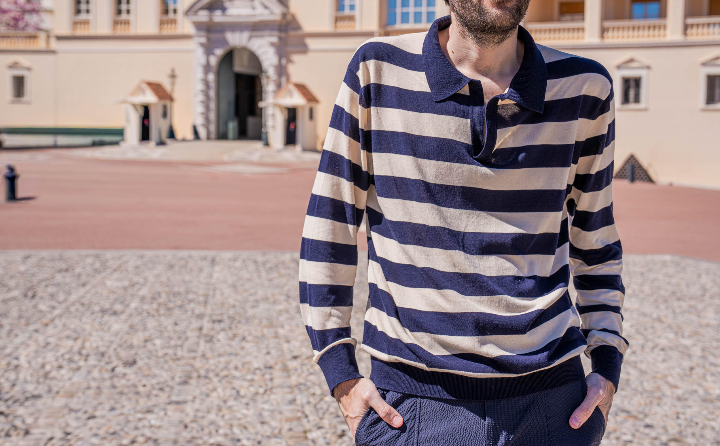 Marko Tadić, founder of the Mr.M blog, smiling in a FERRAGAMO navy striped silk knit polo in front of the pink Belle Epoque facade and glass canopy on the palace square in Monaco