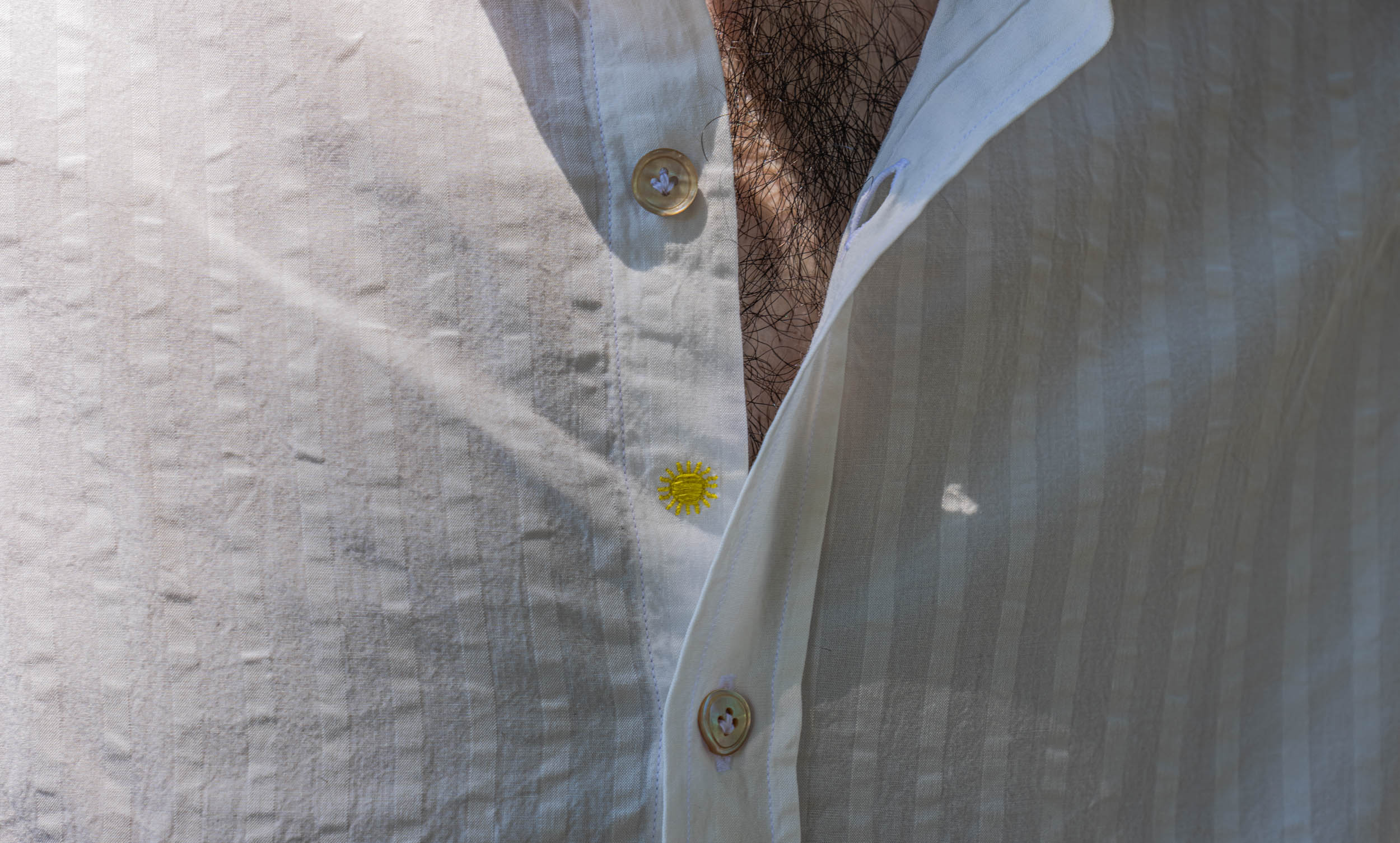 Macro detail of the embroidered yellow sun beside mother-of-pearl buttons on Marko Tadić's Giannetto Portofino lyocell mandarin collar shirt