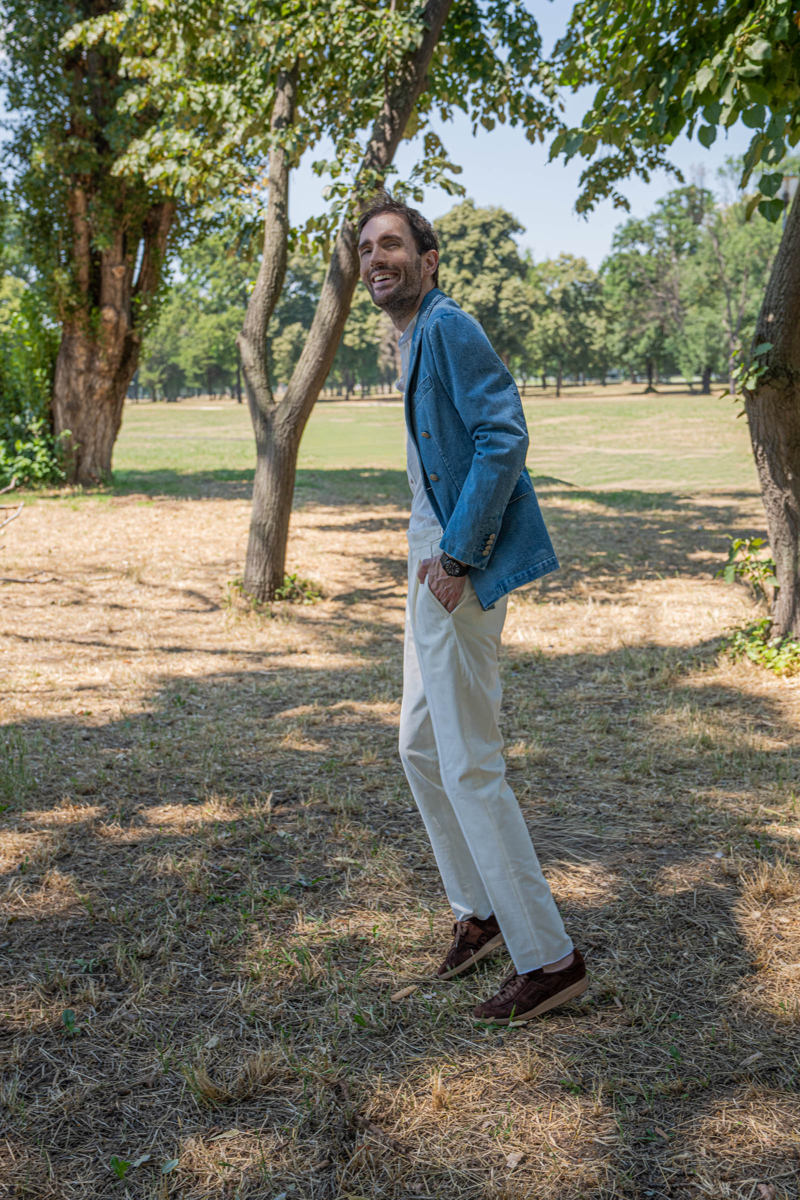 Relaxed full-length pose by Marko Tadić in a finely striped white lyocell shirt tucked into high-waisted cream trousers with side adjusters and brown suede trainers