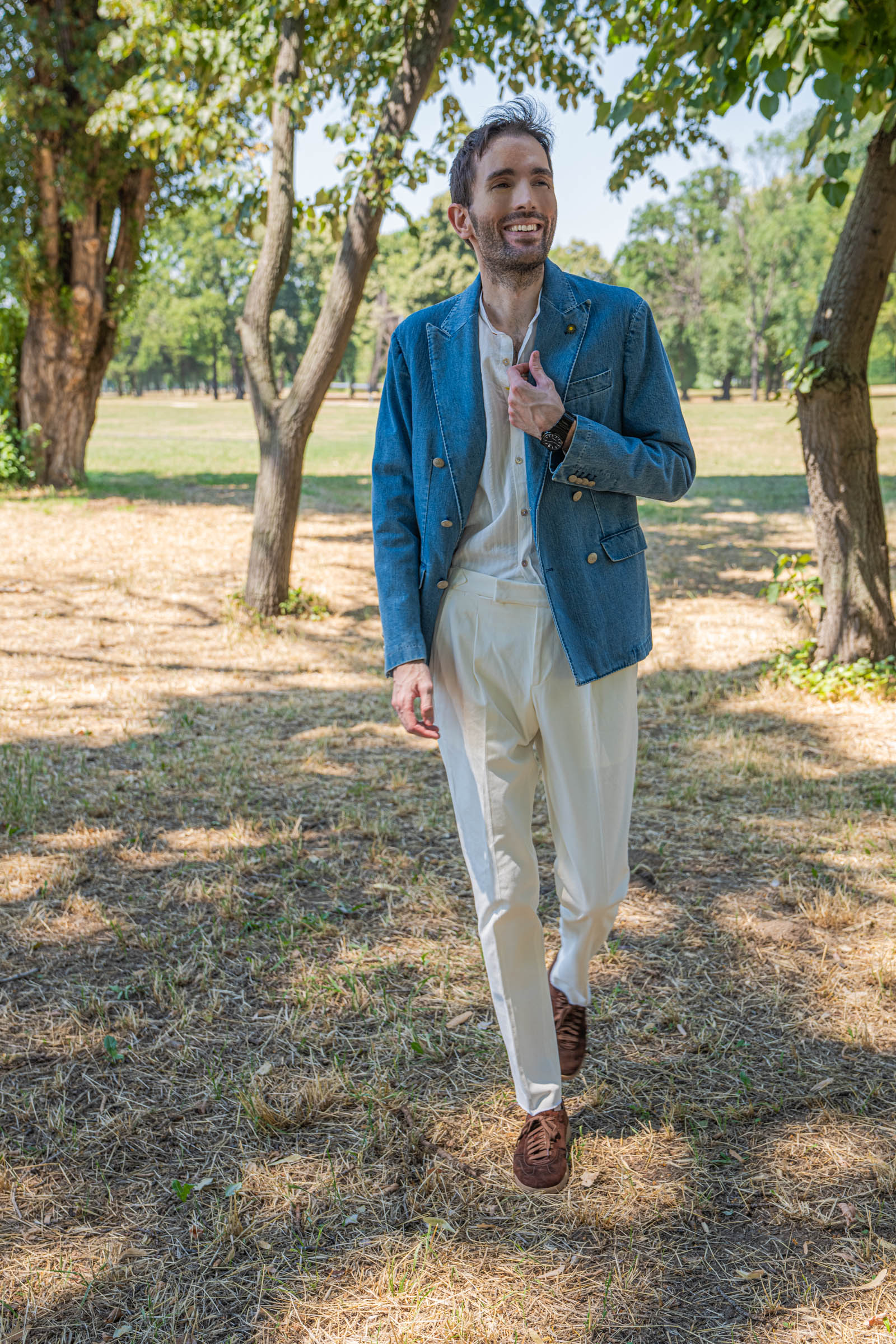 Marko Tadić standing beside an old tree in a tailored denim blazer and white band collar shirt, a black integrated bracelet watch on his wrist