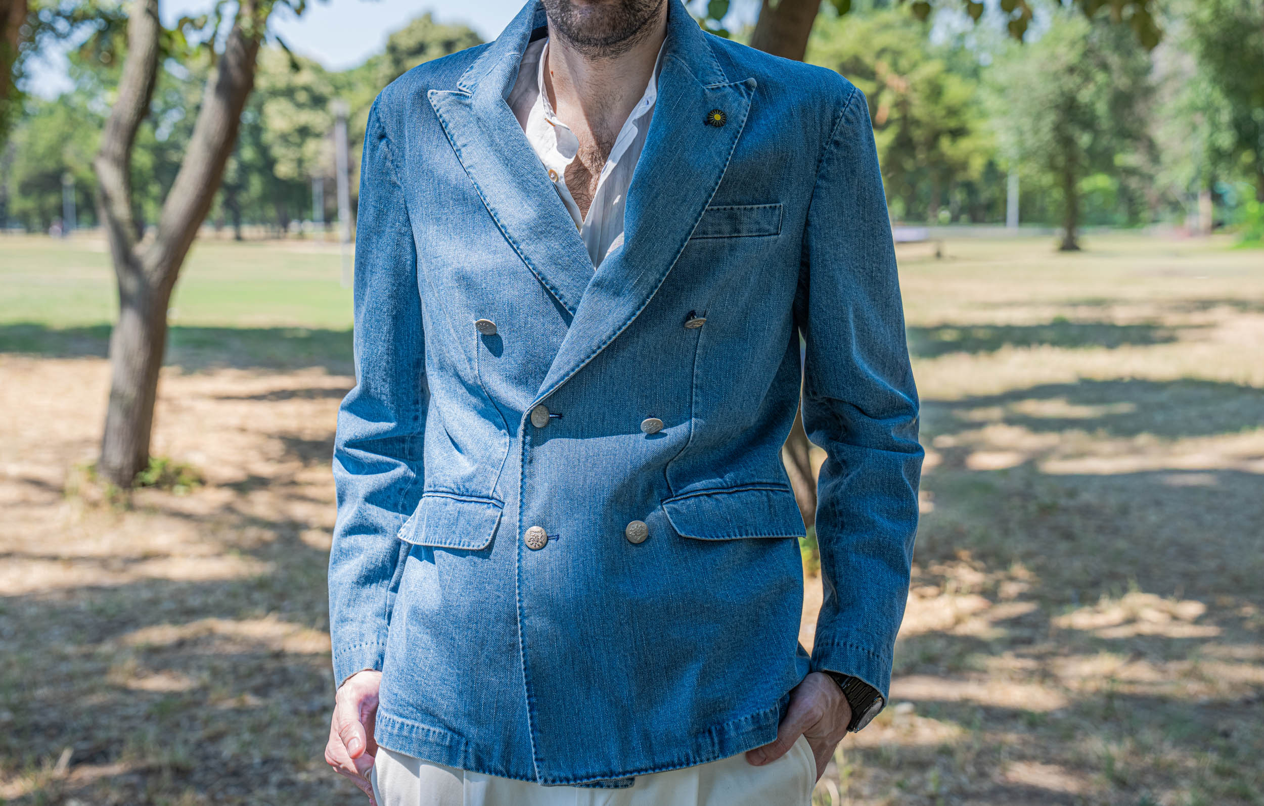 Detail of Marko Tadić's double-breasted denim blazer by Giannetto Portofino with hand-sewn metal buttons, peak lapels and a yellow sun lapel pin