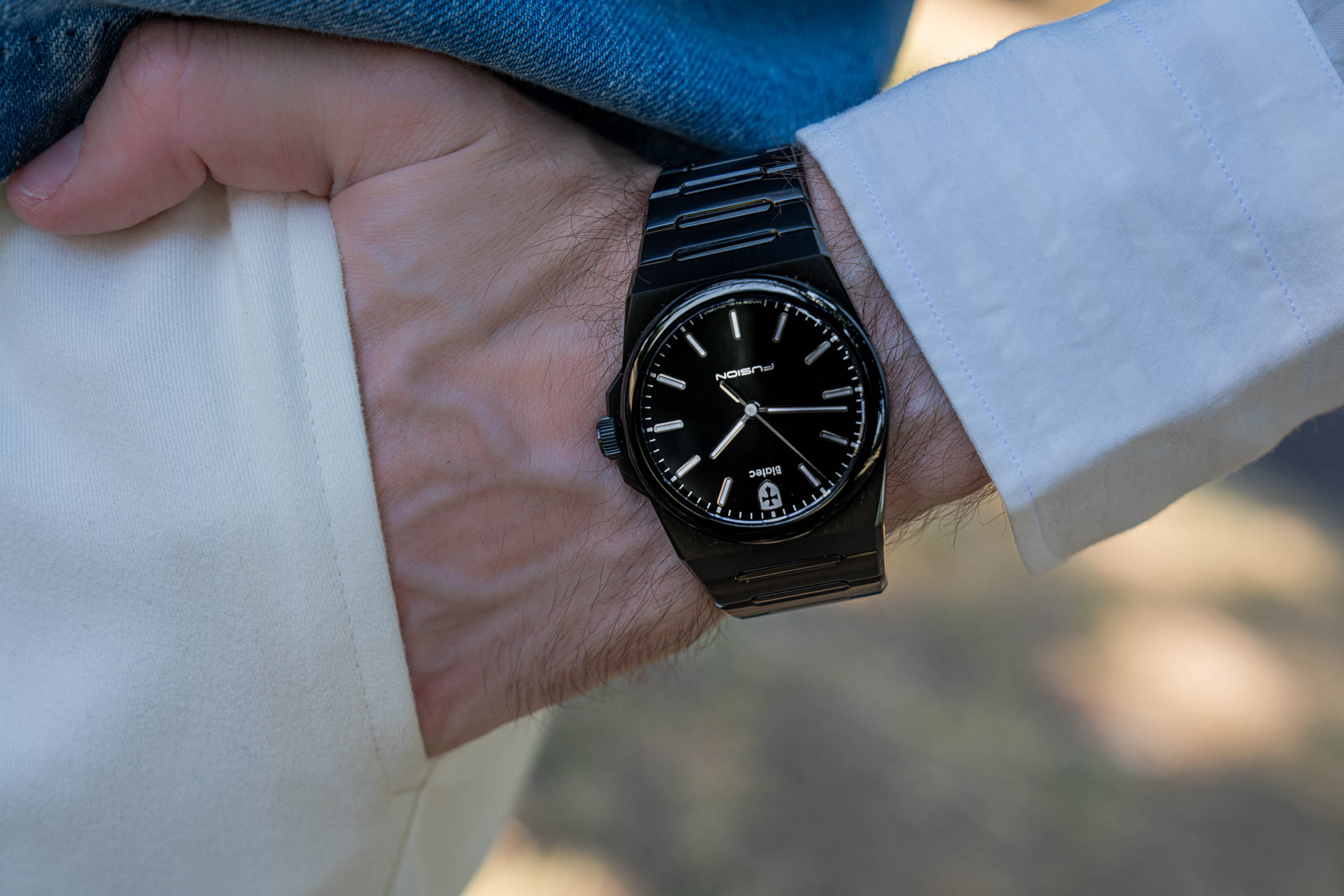 Marko Tadić's Biatec Fusion 03 watch with a black lacquered dial and DLC coated bracelet photographed against cream trousers and a denim cuff