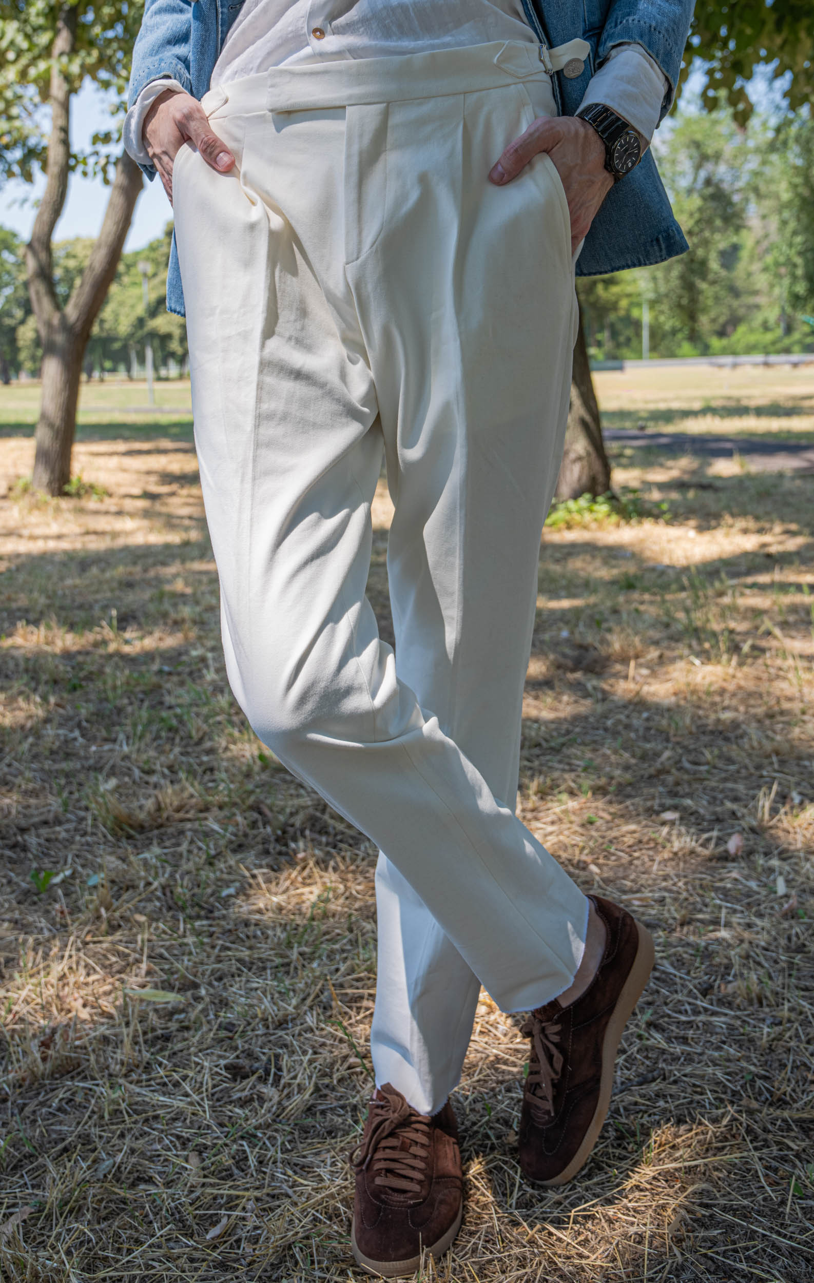 Lower-body detail of Marko Tadić's cream Cifonelli high-waisted trousers with a clean tapered leg breaking over brown suede sneakers