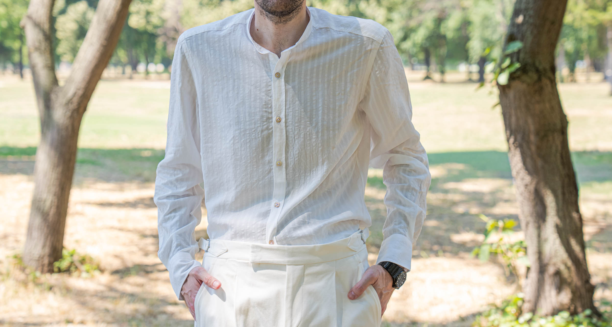 Close-up of Marko Tadić's natural white lyocell shirt with fine woven stripes tucked into high-rise cream trousers fitted with silver side adjusters