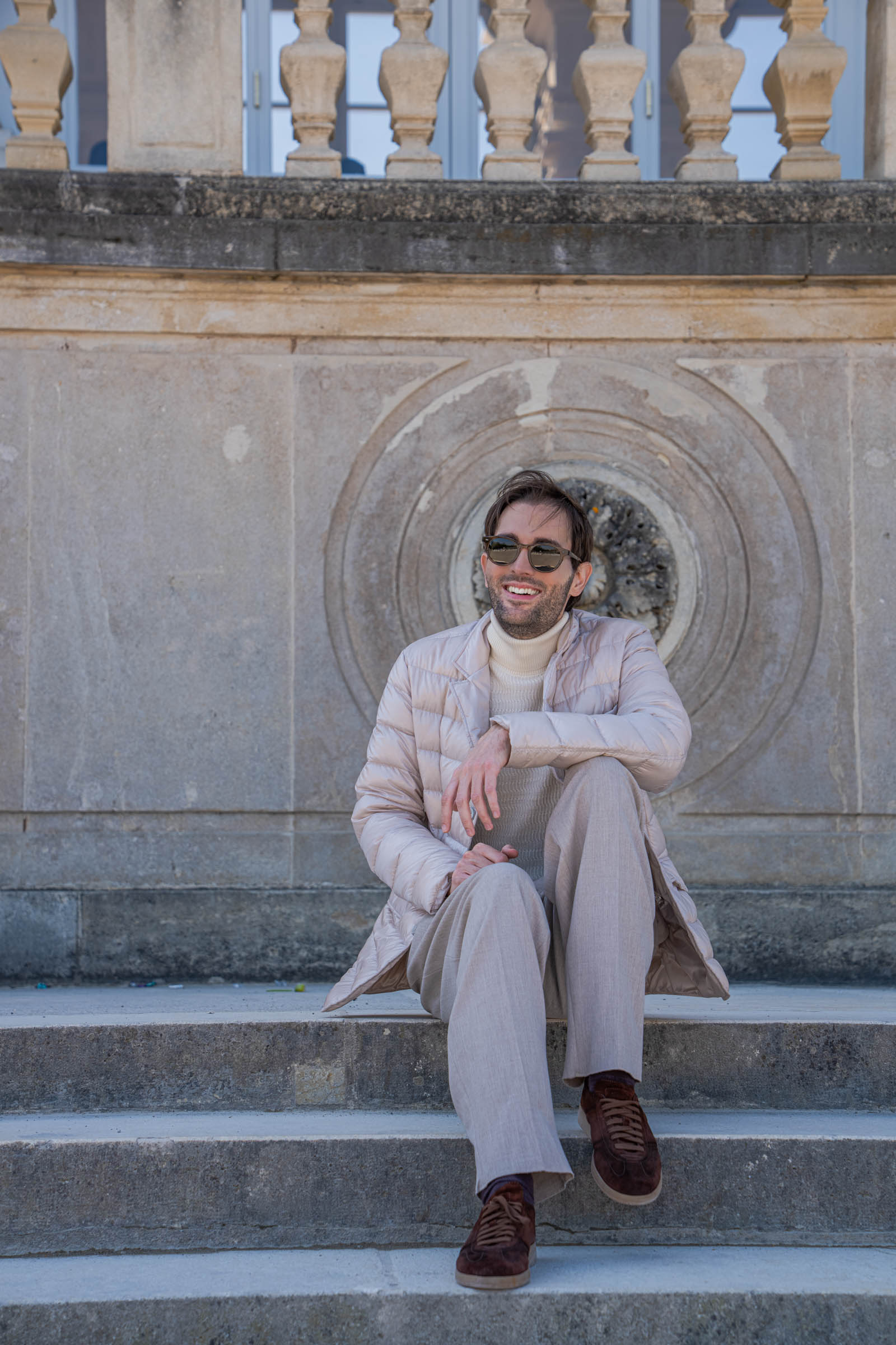 Marko Tadić, founder of the Mr.M blog, sitting on the stone steps of the Gloriette in a Herno jacket and Giorgio Armani beige outfit