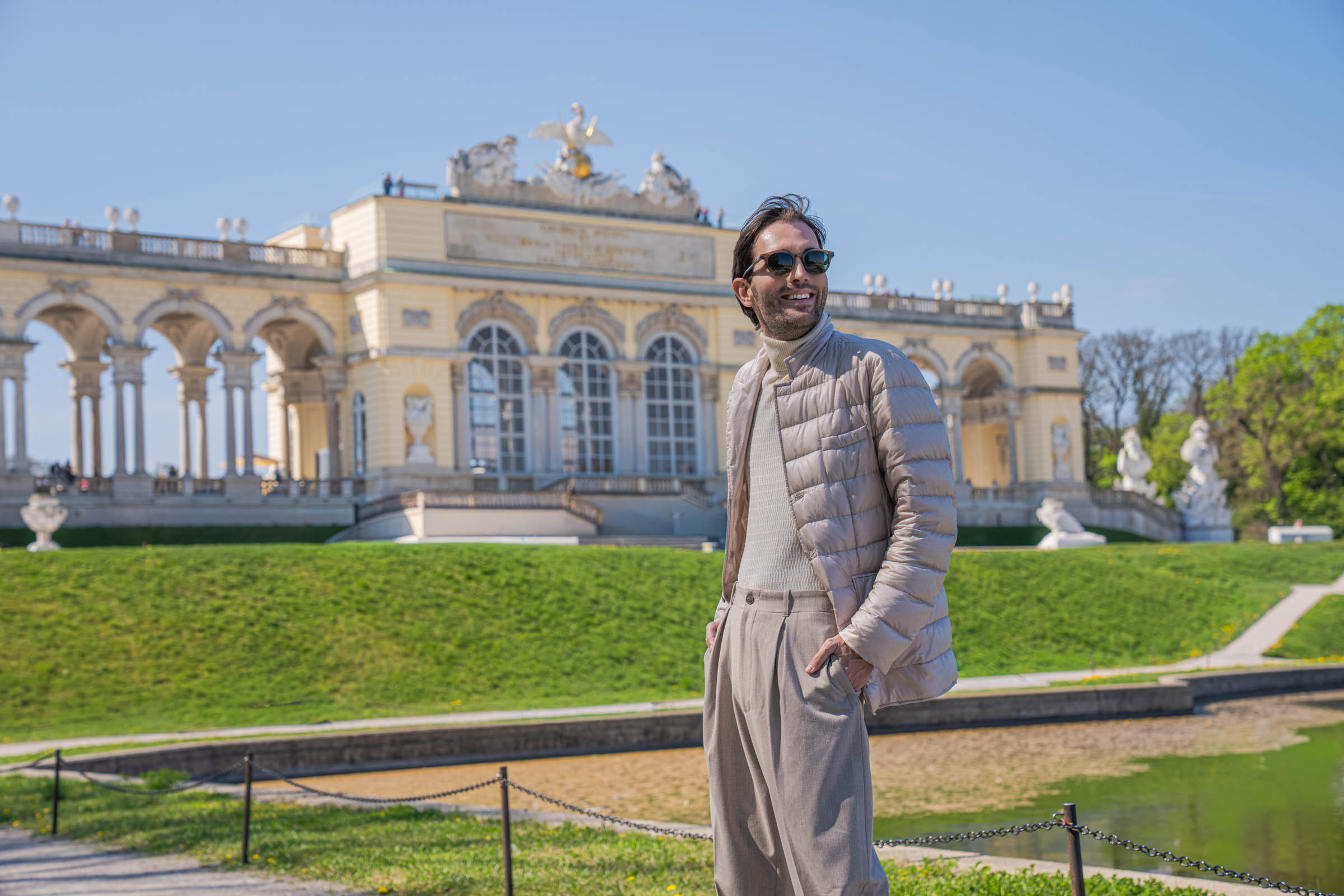 Marko Tadić, founder of the Mr.M blog, smiling over his shoulder in a pearl Herno down jacket by the Gloriette pond at Schönbrunn