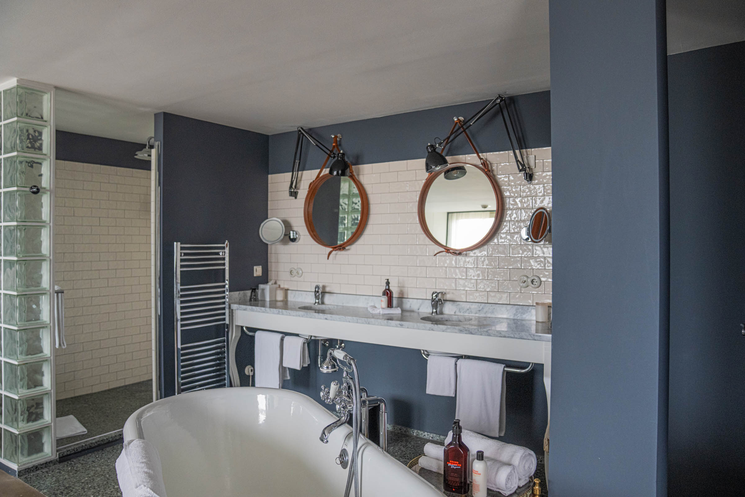 Open-plan suite bathroom at Grand Ferdinand Vienna with marble double sinks, leather-strap mirrors and freestanding tub