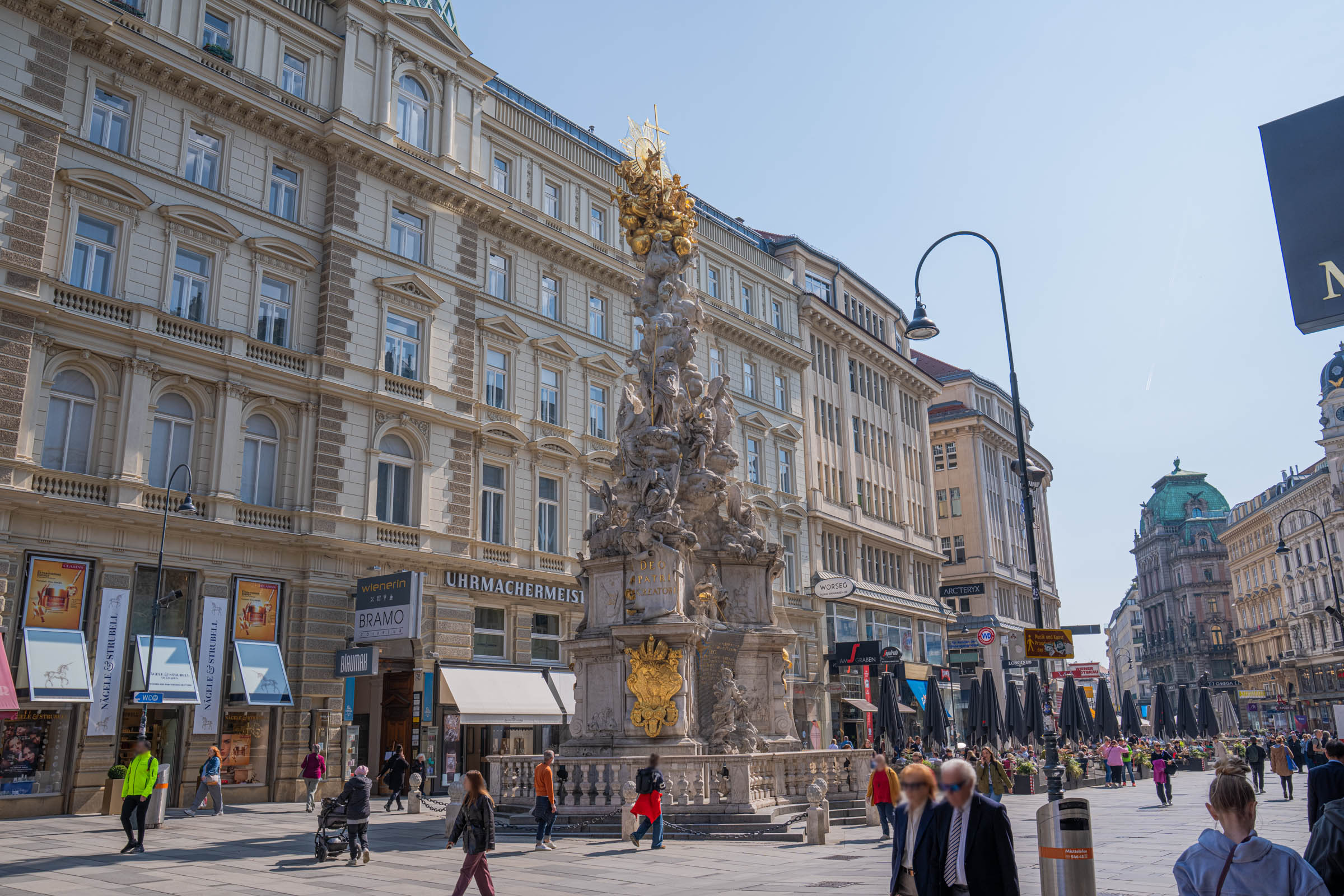 Graben boulevard in Vienna with the baroque Plague Column and historic clock tower on a sunny day