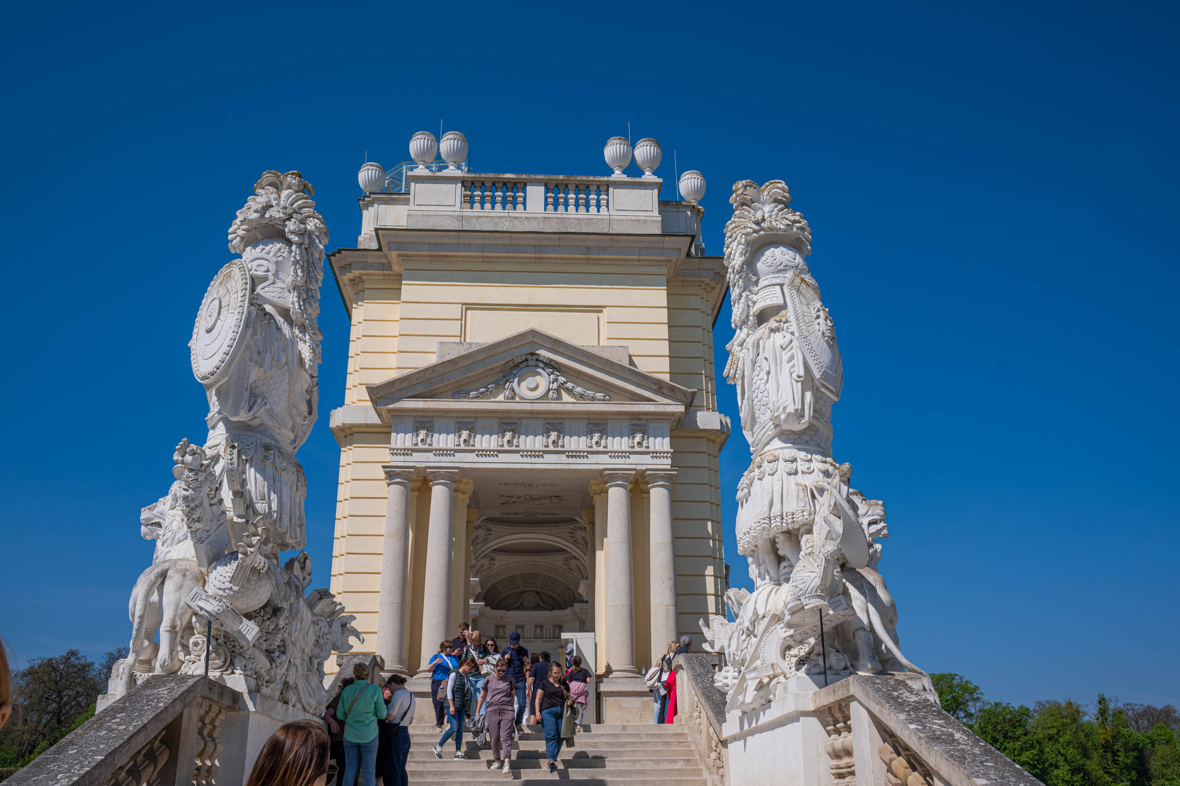 Grand staircase of the Gloriette with baroque trophy sculptures against a deep blue Vienna sky