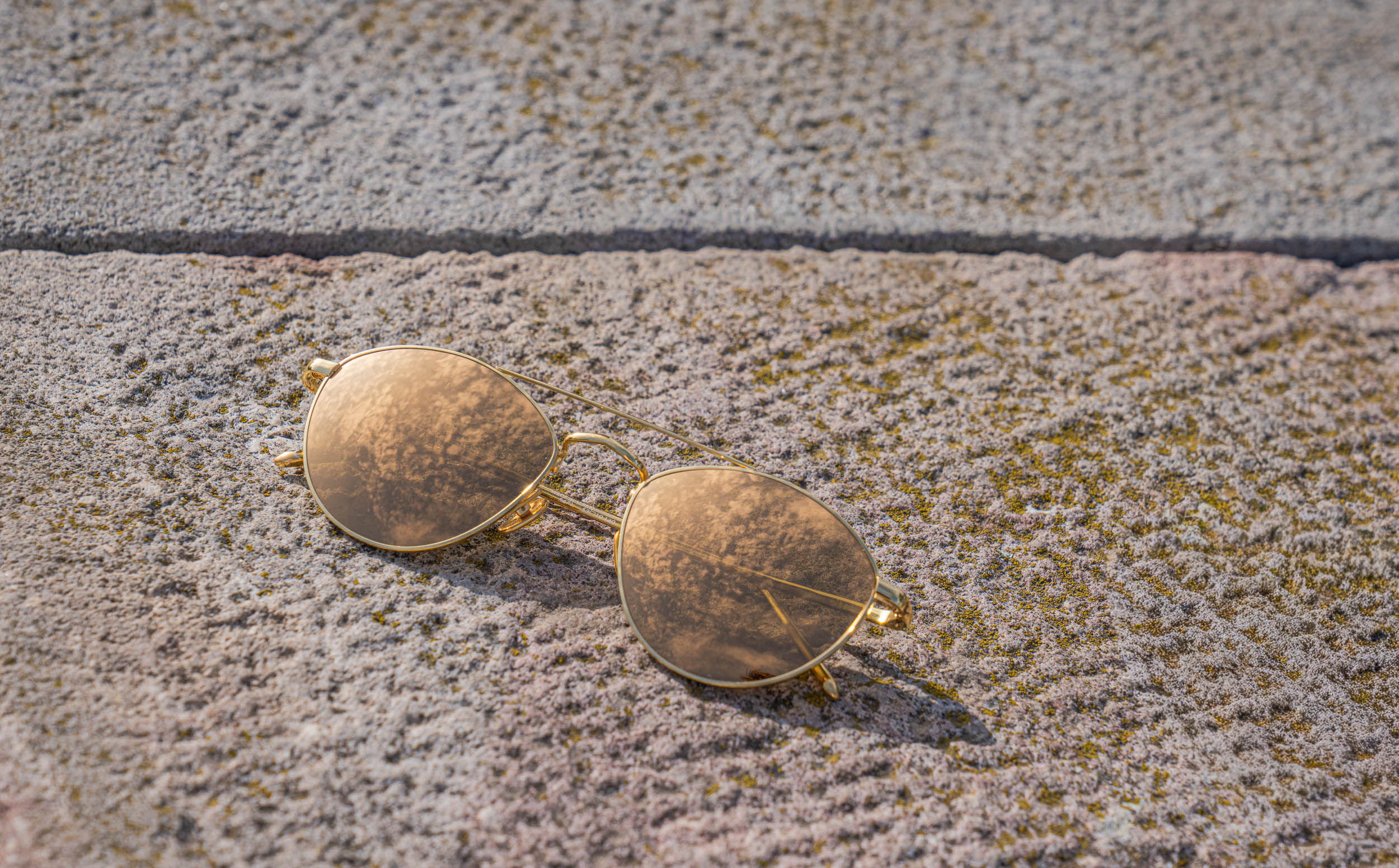 Linda Farrow gold mirrored aviator sunglasses resting on stone at Belgrade Fortress